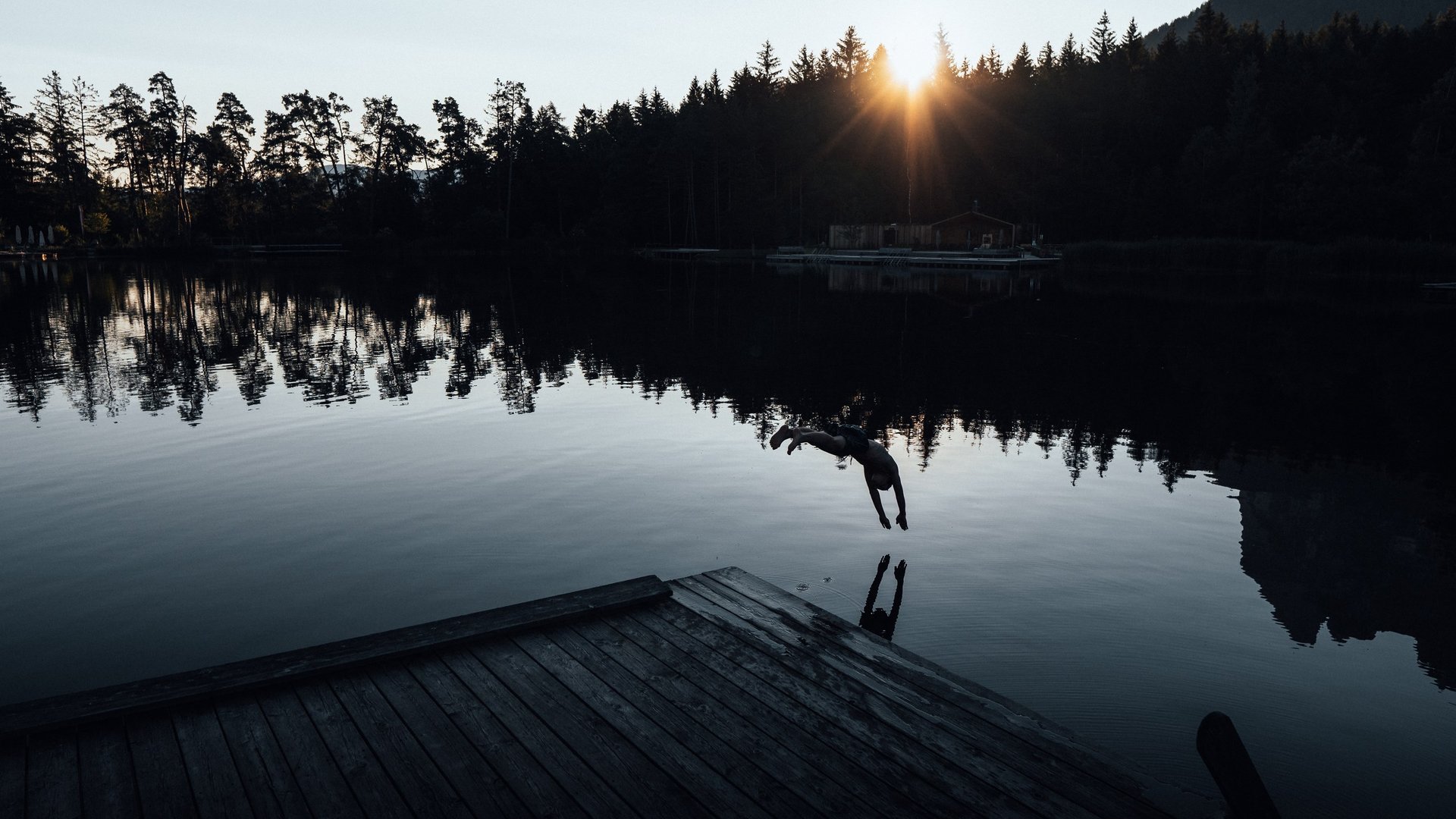 Luoghi di energia Persona che si tuffa nel lago con tramonto e alberi sullo sfondo