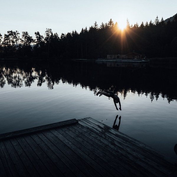 Sensoria Dolomites: Wellnesshotel in den Dolomiten Person beim Sprung ins Wasser am See mit Sonnenuntergang und Wald im Hintergrund