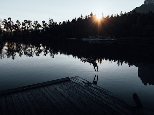 Sustainability at Sensoria Dolomites Person diving into lake with sunset and trees in the background