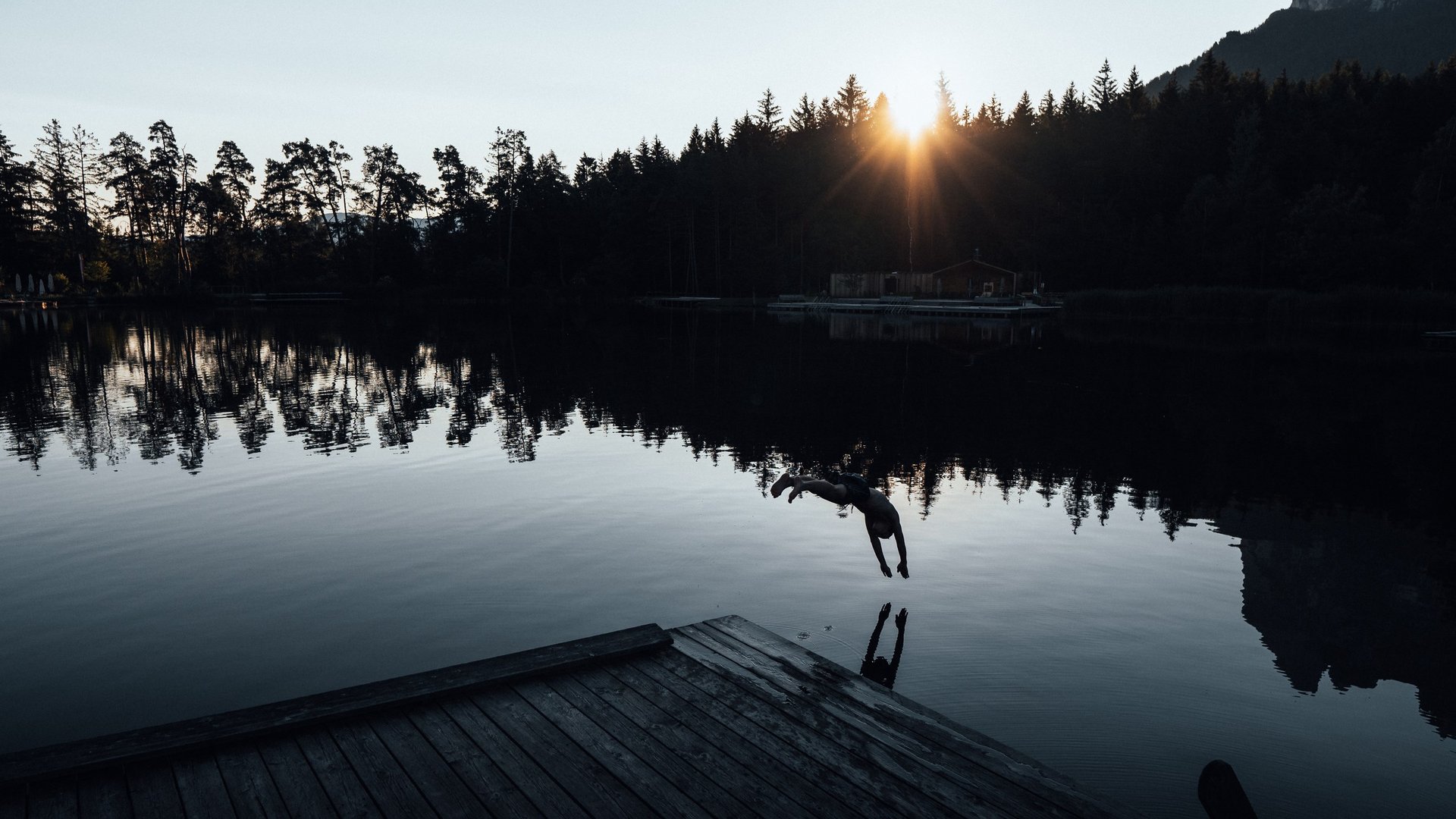 Hotel all’Alpe di Siusi: un tempio di energia per l’anima Persona che si tuffa nel lago con tramonto e alberi sullo sfondo