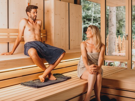 Kostbare Augenblicke in Ihrem Romantikhotel in den Dolomiten Mann und Frau entspannen in einer Holzsauna mit Fenster und Blick ins Grüne