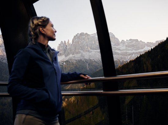 Kraftorte in Südtirol Frau blickt von einer Aussichtsplattform auf bewaldete Berge und Felsgipfel