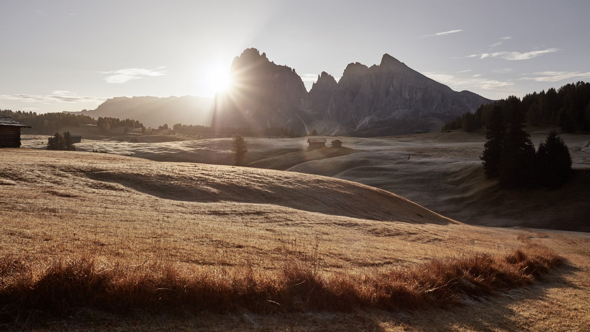 Sensoria Dolomites: much more than a hotel in South Tyrol Sunrise over rolling meadow with wooden huts and mountains in the background