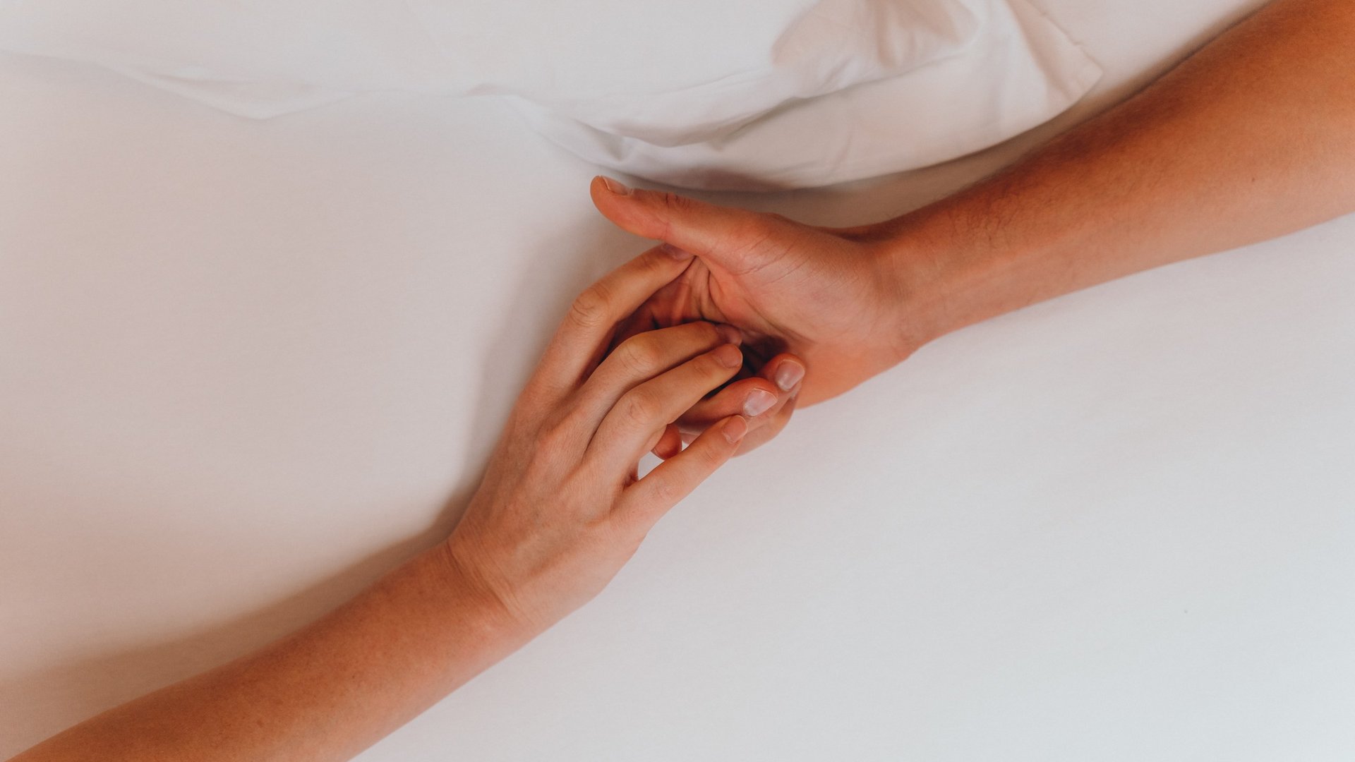 Kostbare Augenblicke in Ihrem Romantikhotel in den Dolomiten Zwei Hände, die sich sanft auf einem weißen Bett berühren