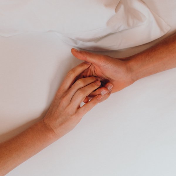 Romantischer Kurzurlaub für Verliebte – Sensoria Dolomites Zwei Hände, die sich sanft auf einem weißen Bett berühren