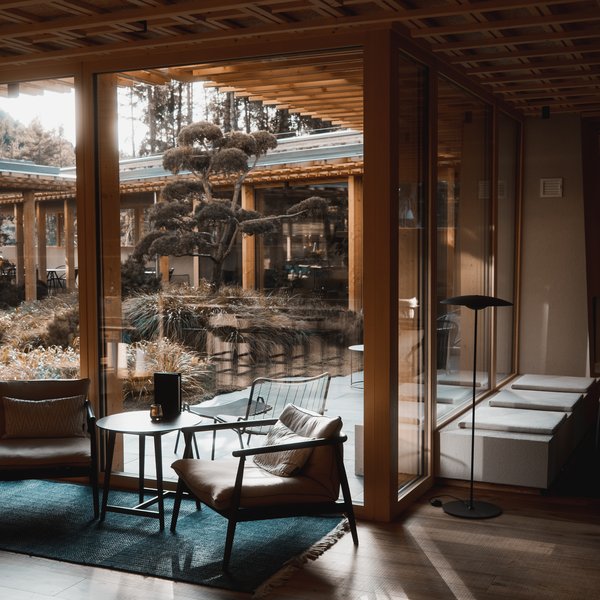 Sensoria Dolomites: Babymoon in Südtirol Gemütlicher Sitzbereich mit Stühlen und Tisch vor großen Fenstern und Blick auf Garten