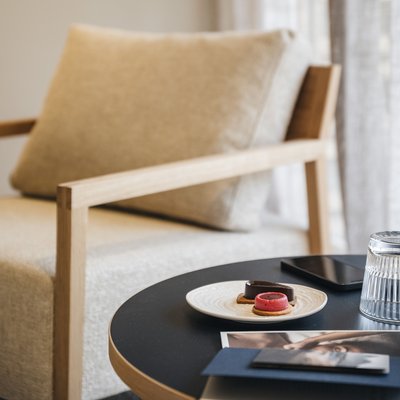 Essence single room North Side table with cookies, glass, and phone in front of a beige armchair