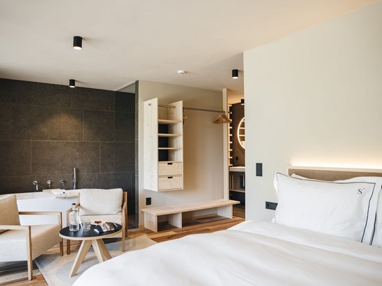 Sensoria Dolomites – Urlaub in Seis am Schlern Modernes Hotelzimmer mit Bett, Sitzecke, Badewanne und offenem Kleiderschrank