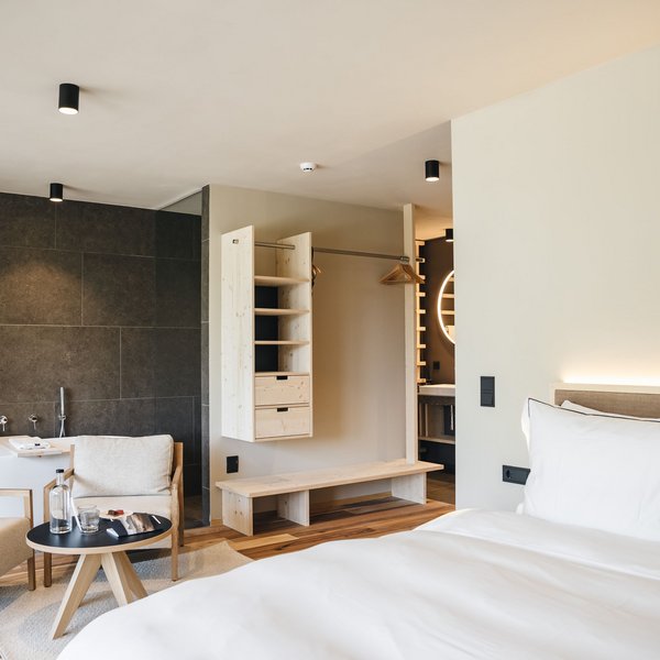 Sensoria Dolomites: Flitterwochen in Südtirol Modernes Hotelzimmer mit Bett, Sitzecke, Badewanne und offenem Kleiderschrank
