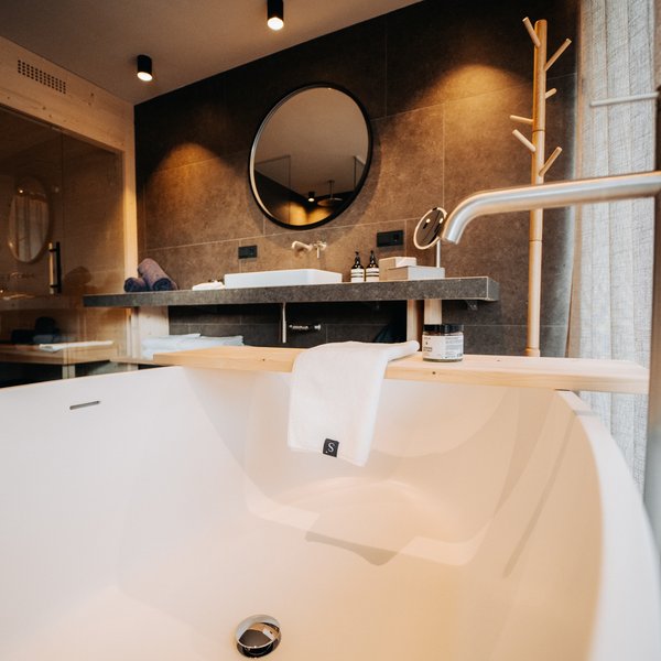 Sensoria: Private Spa Suite mit Whirlpool in Südtirol Moderne Badewanne mit Holzablage und rundem Spiegel im stilvollen Badezimmer