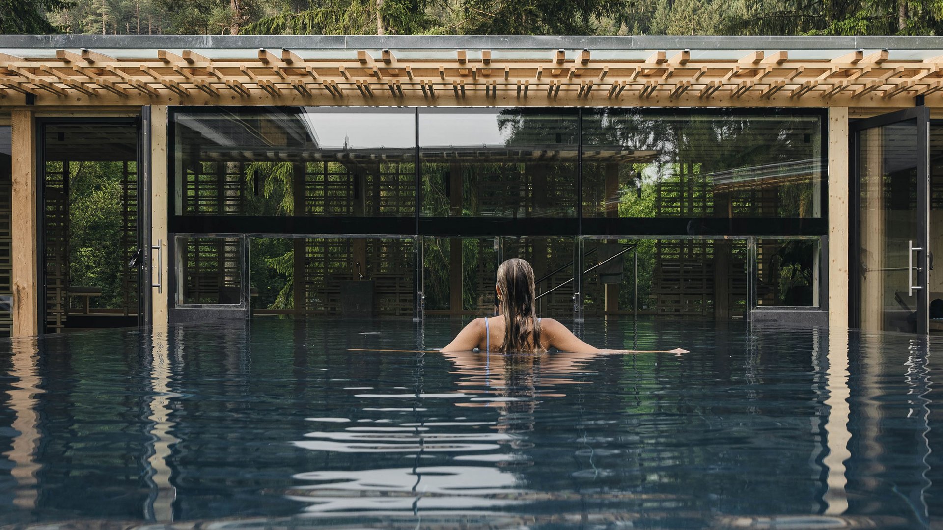 Wellness Aphrodite: Sensoria Dolomites among the winners Woman in pool facing glass building with mountains and trees in background