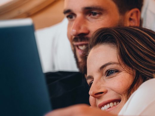 Inklusivleistungen – last minute nach Südtirol Paar liegt zusammen und sieht lächelnd auf einen Laptop