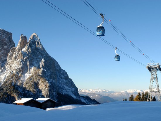 Mehr als ein Hotel im Naturpark Schlern-Rosengarten Seilbahn über schneebedeckten Bergen und Hütten bei klarem Himmel