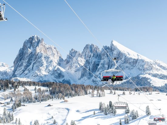 Active holidays in South Tyrol – ready for pure nature? Ski lift with skiers in front of snowy mountains and clear blue sky