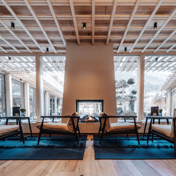 Sensoria Dolomites: il vostro hotel sull’Alpe di Siusi Lounge moderna con camino, soffitto in legno e grandi vetrate con vista sulle montagne