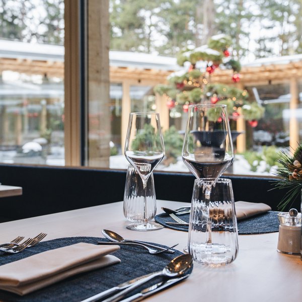Hotel gourmet in Alto Adige: Sensoria Dolomites Tavolo apparecchiato con calici da vino davanti a una finestra con albero di Natale