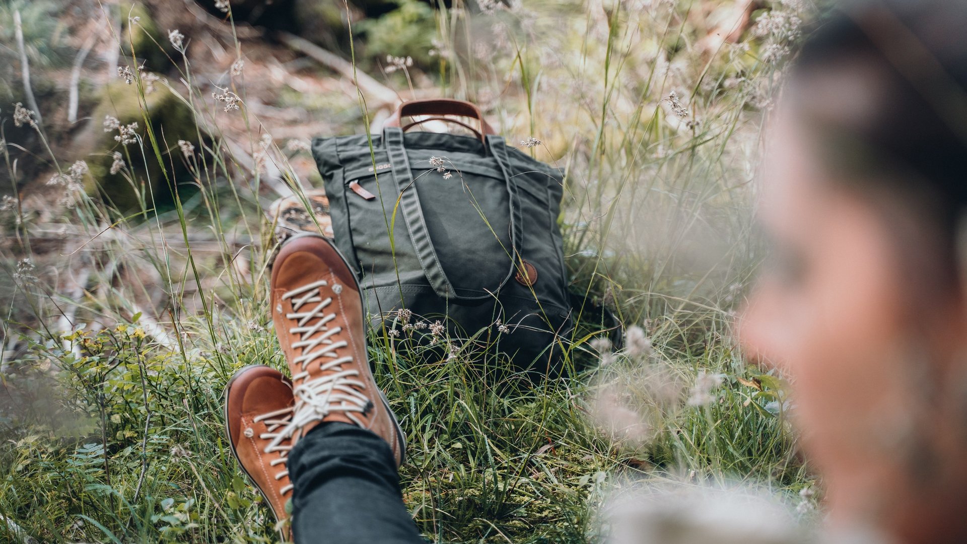 A summer holiday in the mountains Person wearing hiking boots sitting on grass beside a backpack in nature