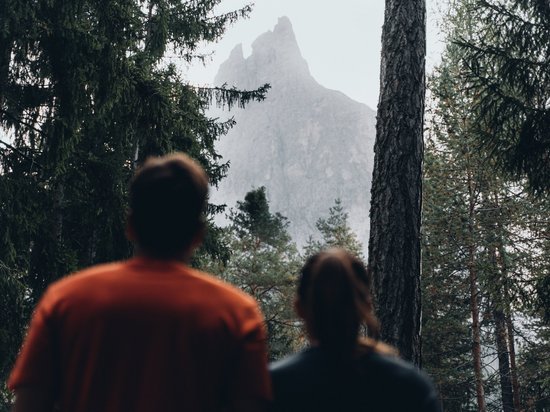 Holidays in the Dolomites – holidays at Sensoria Dolomites Two people looking at a tall mountain peak through the forest