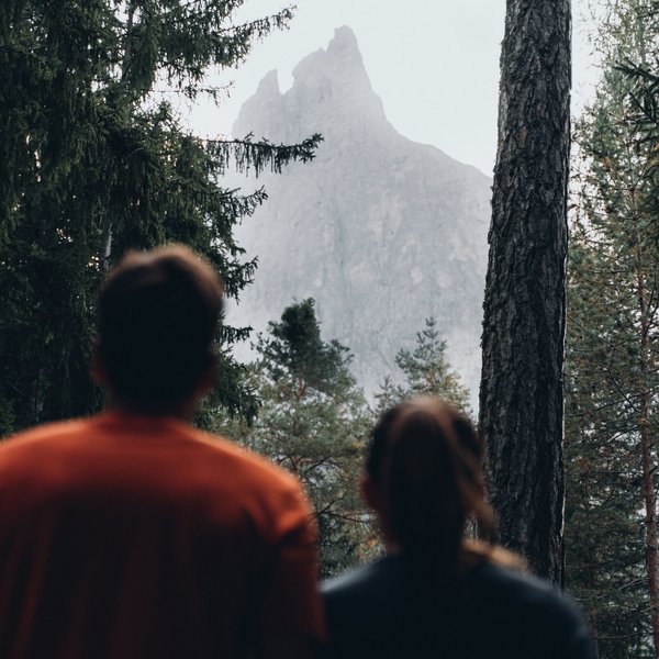 Active holidays in South Tyrol – ready for pure nature? Two people looking at a tall mountain peak through the forest