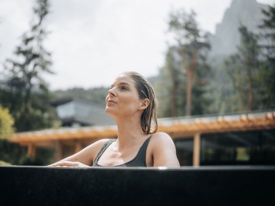 Hotel all’Alpe di Siusi: un tempio di energia per l’anima Donna rilassata in jacuzzi all'aperto con vista su foresta e montagne