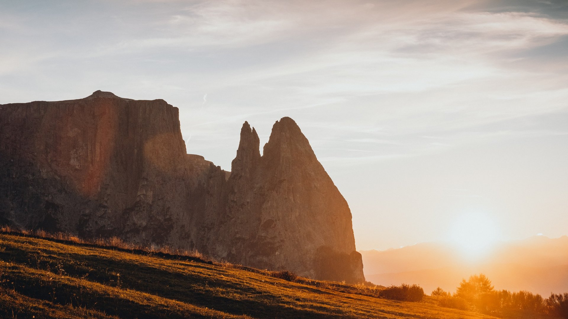 Scopri Sciliar: Avventure e Escursioni nel Cuore delle Dolomiti Tramonto arancione sulle montagne e su un prato