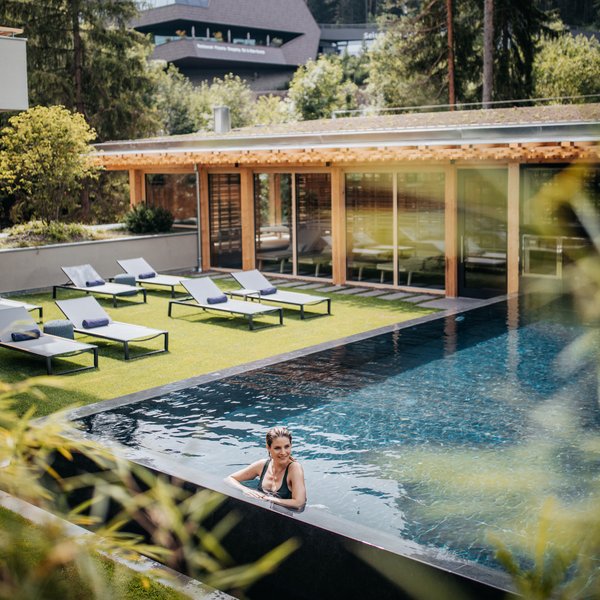 Sensoria Dolomites: Babymoon in Südtirol Frau entspannt im Pool eines modernen Spas mit Liegestühlen und Wald im Hintergrund