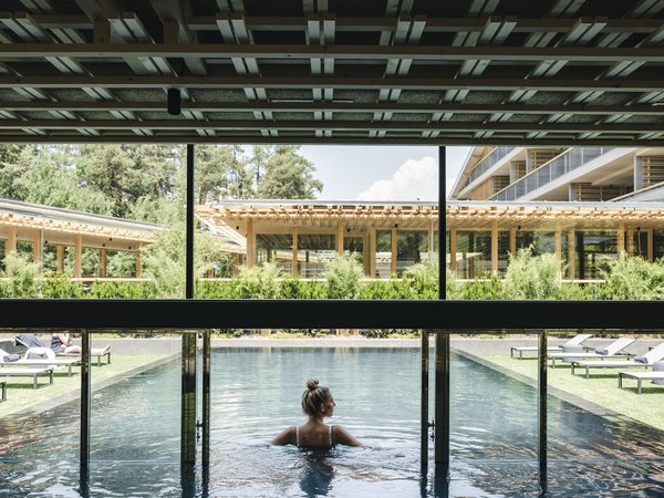 Wellness Aphrodite: Sensoria Dolomites among the winners Woman standing in hotel outdoor pool with modern wooden architecture background