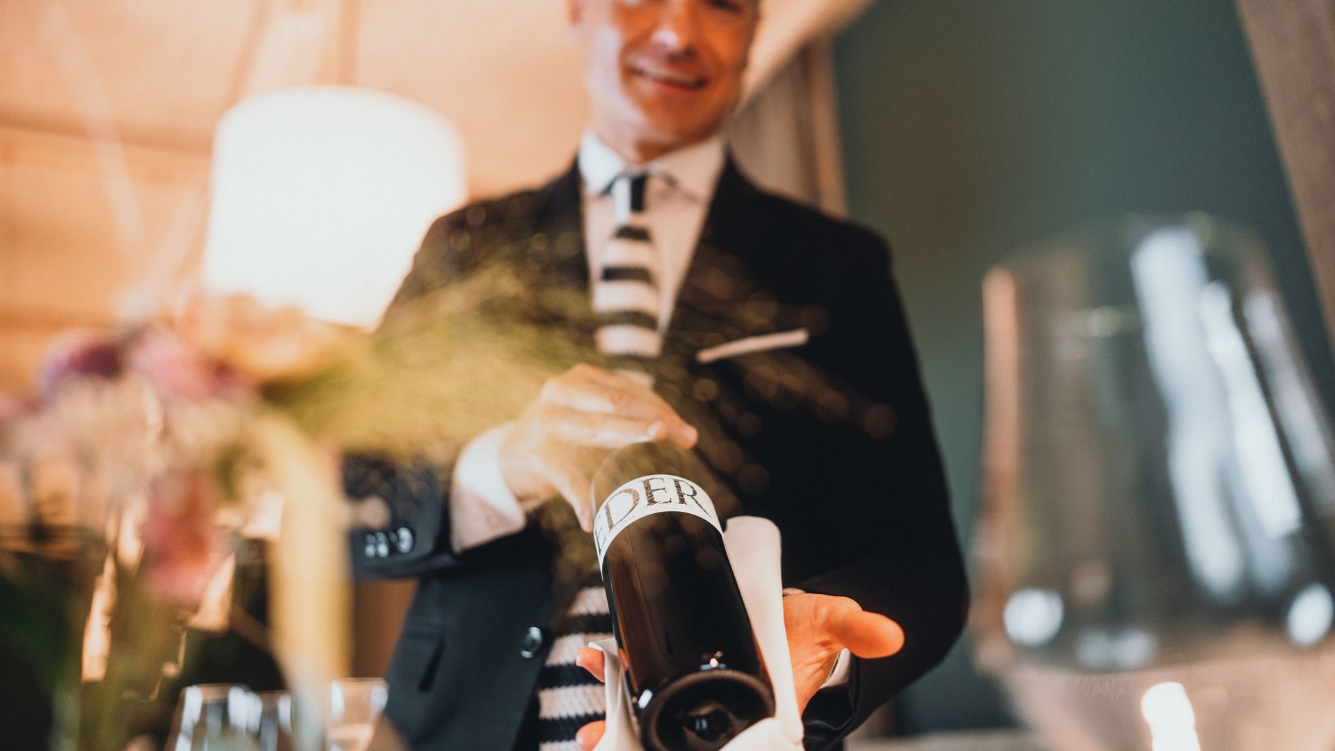 Hotel gourmet in Alto Adige: Sensoria Dolomites Uomo che serve una bottiglia di vino in un ristorante
