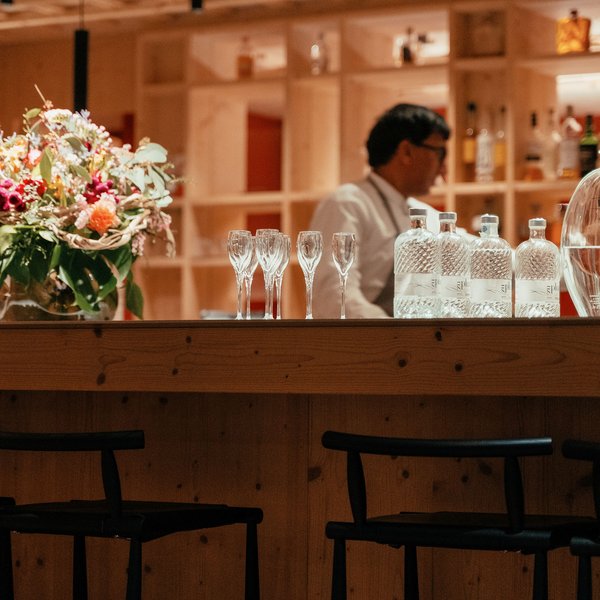 Genussurlaub in Südtirol – Sensoria Dolomites Bar mit Gläsern, Flaschen und Blumenstrauß, Barkeeper im Hintergrund