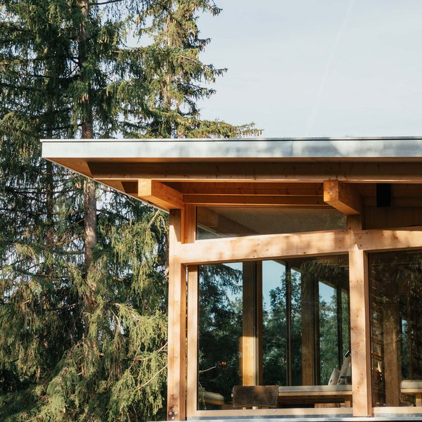 Sensoria Dolomites: Wellnesshotel in den Dolomiten Modernes Holzhaus mit großen Fenstern neben hohen Kiefern im Wald