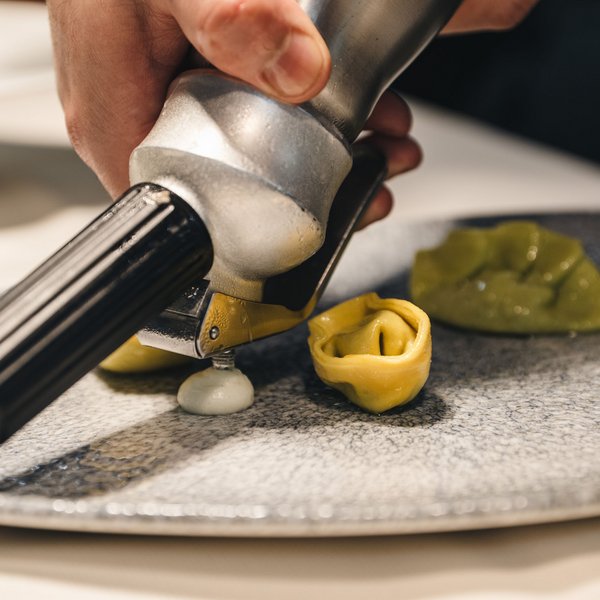 Genussurlaub in Südtirol – Sensoria Dolomites Eine Hand spritzt Sauce auf selbstgemachte gefüllte Pasta auf einem Teller