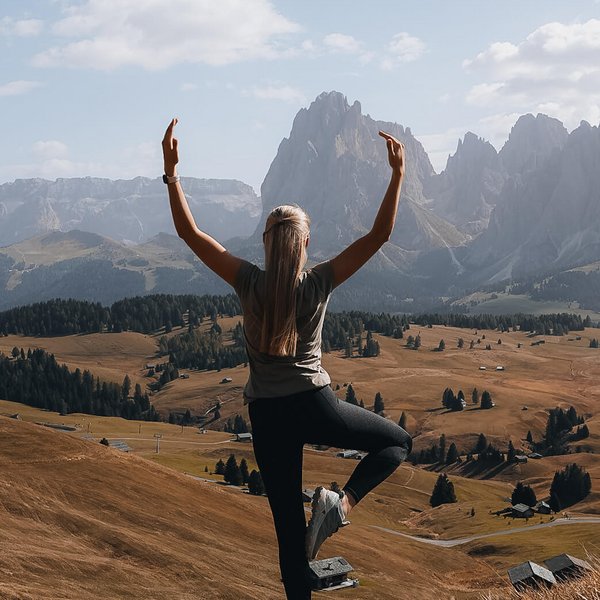 Sensoria Dolomites: Wellnesshotel in den Dolomiten Frau macht Yoga im Gebirge mit Blick auf Tal und Berge bei klarem Himmel