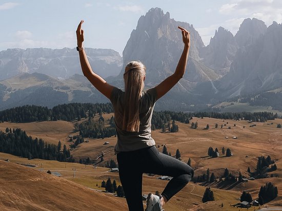 Vacanza di yoga in Trentino-Alto Adige Donna fa yoga sulle montagne con vista sulla valle e cielo sereno