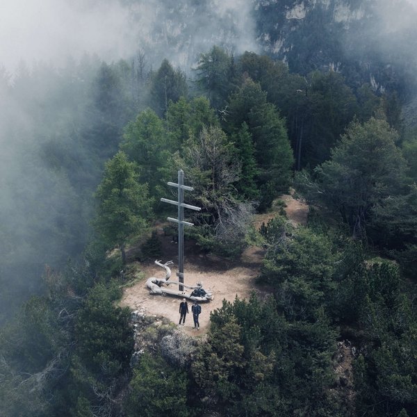 Active holidays in South Tyrol – ready for pure nature? Two people beside a summit cross on a foggy mountain surrounded by trees
