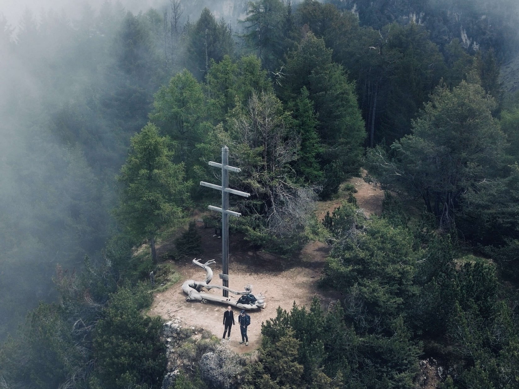 Offers – holidays in the Dolomites UNESCO World Heritage Two people beside a summit cross on a foggy mountain surrounded by trees
