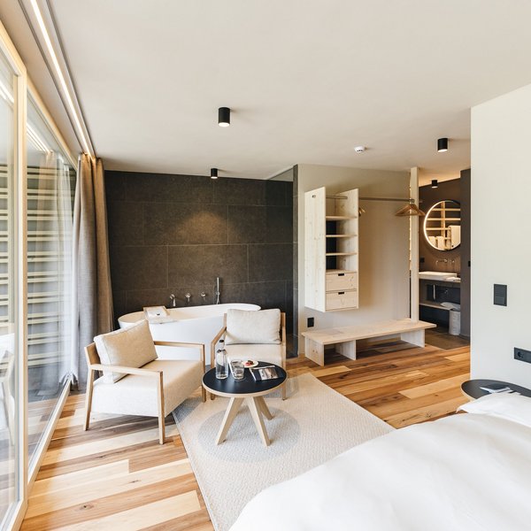 Sensoria Dolomites: Babymoon in Südtirol Modernes Hotelzimmer mit Bett, Sitzbereich, Badewanne und Holzboden