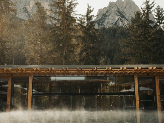 Sensoria Dolomites: your hotel in the Italian Alps Modern wooden building with glass front, misty pool, and mountain background