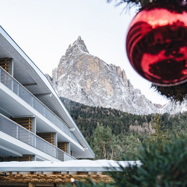 Sensoria Dolomites: il vostro hotel sull’Alpe di Siusi Montagna innevata dietro edificio moderno e albero di Natale con pallina rossa