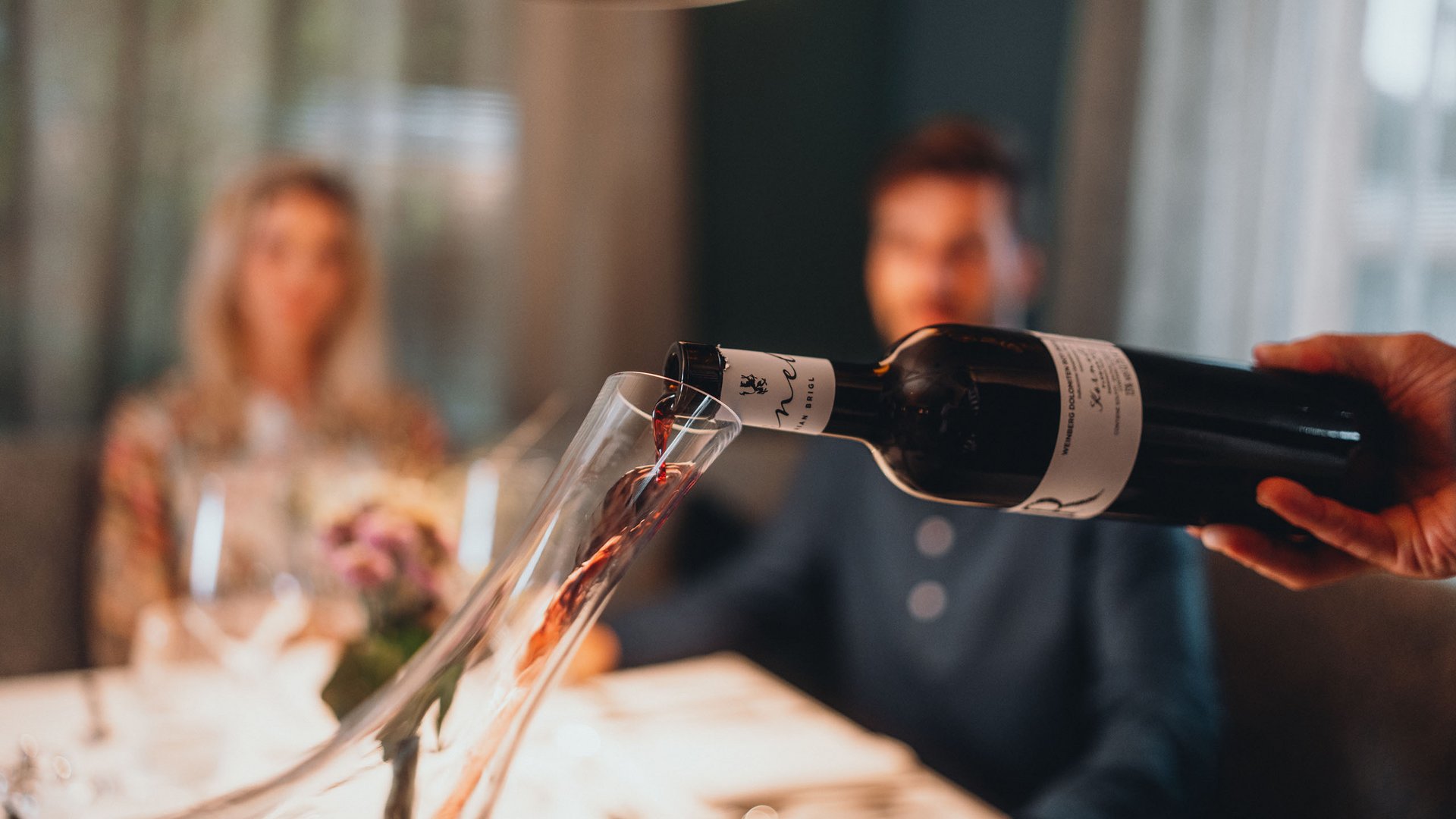 South Tyrolean recipes. Reinterpreted. Red wine being poured into a decanter with blurred people in background