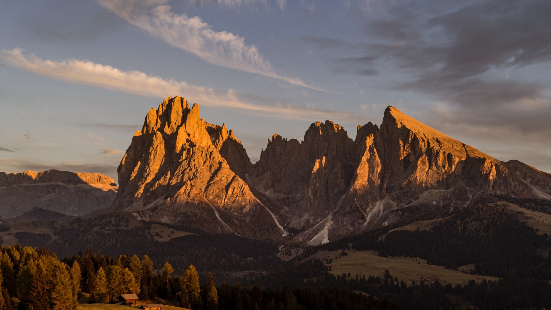 Sensoria Dolomites – holidays in Seis am Schlern Rocky mountain peaks bathed in warm sunset light with forested hills in foreground