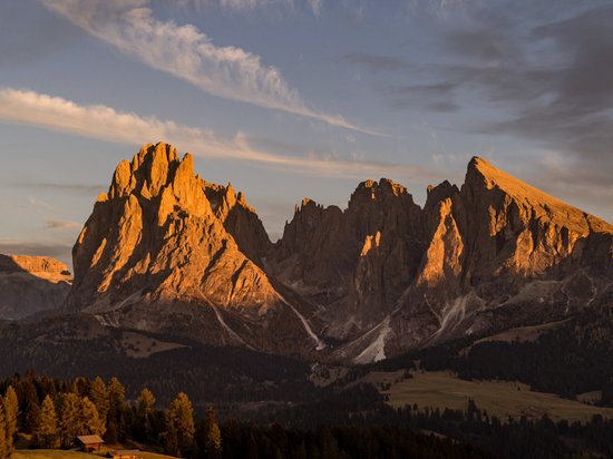 Angebote – Urlaub im Dolomiten UNESCO Welterbe Felsige Bergspitzen in warmem Abendlicht mit bewaldeten Hügeln im Vordergrund