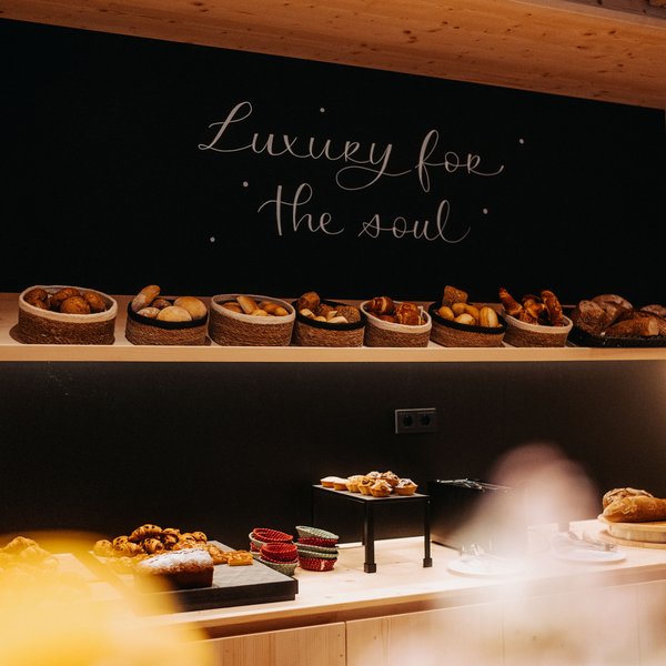 Sensoria Dolomites: Wellnesshotel in den Dolomiten Verschiedene Brote in Körben vor schwarzer Wand mit Schrift Luxury for the soul