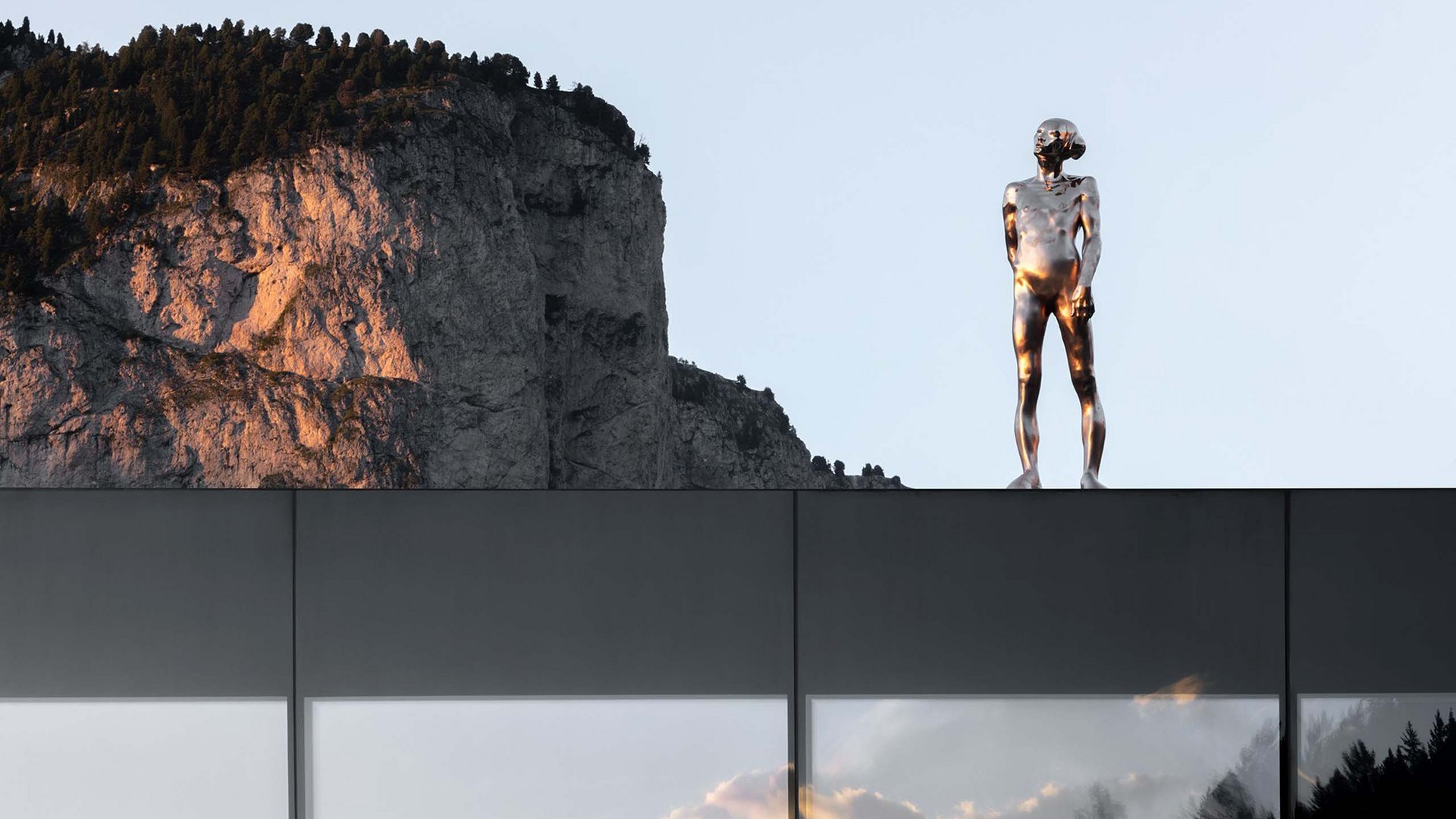 Moderne Skulptur einer glänzenden Figur auf Gebäudedach mit Berg im Hintergrund