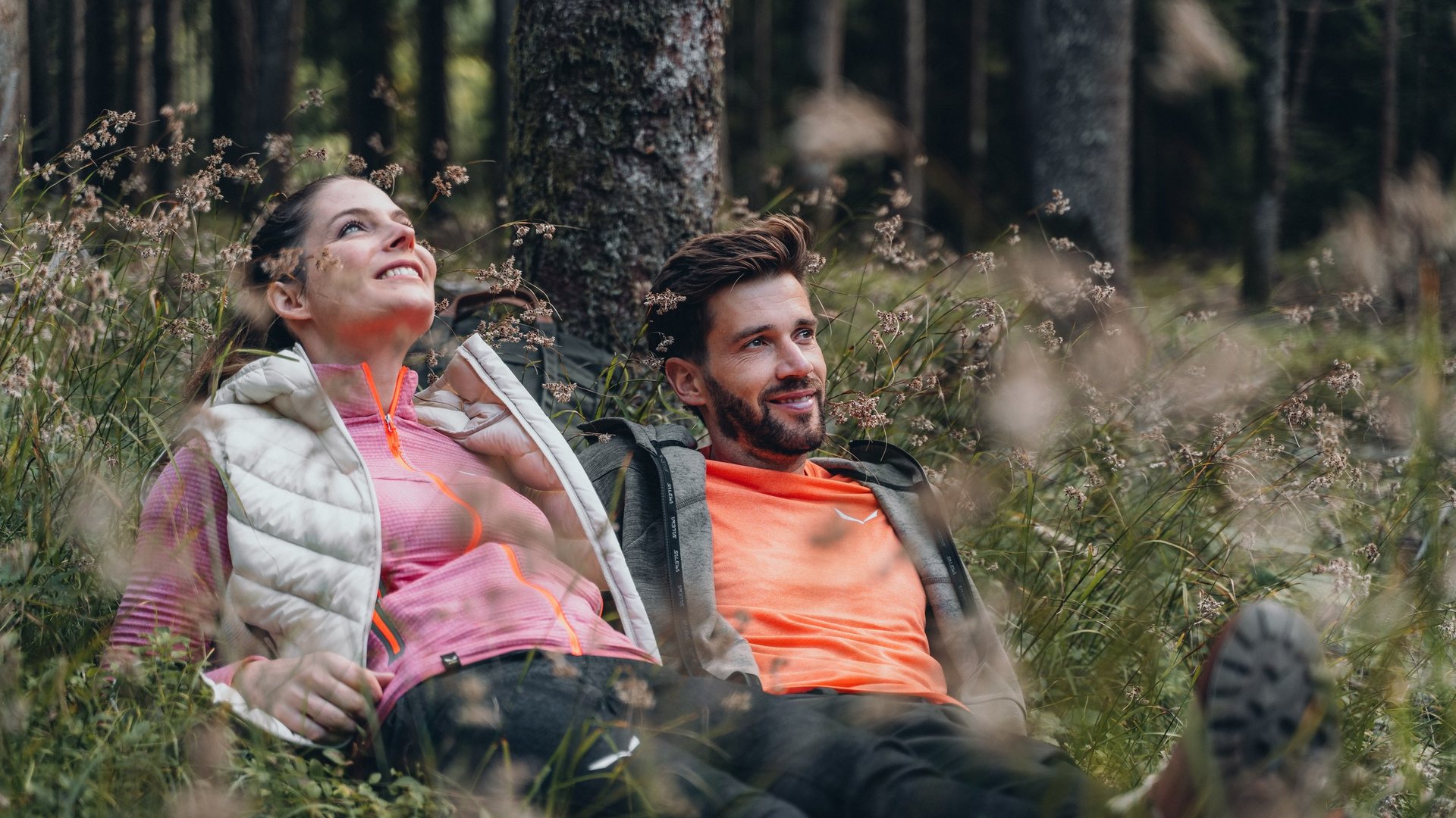 Active holidays in South Tyrol – ready for pure nature? Couple lying on grass in forest looking happily upwards