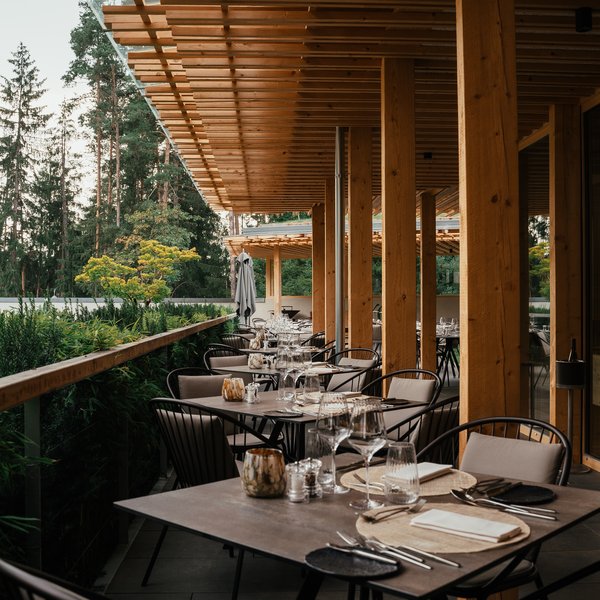 Sensoria Dolomites: Wellnesshotel in den Dolomiten Elegante Außenterrasse eines Restaurants mit gedeckten Tischen aus Holz und Metall