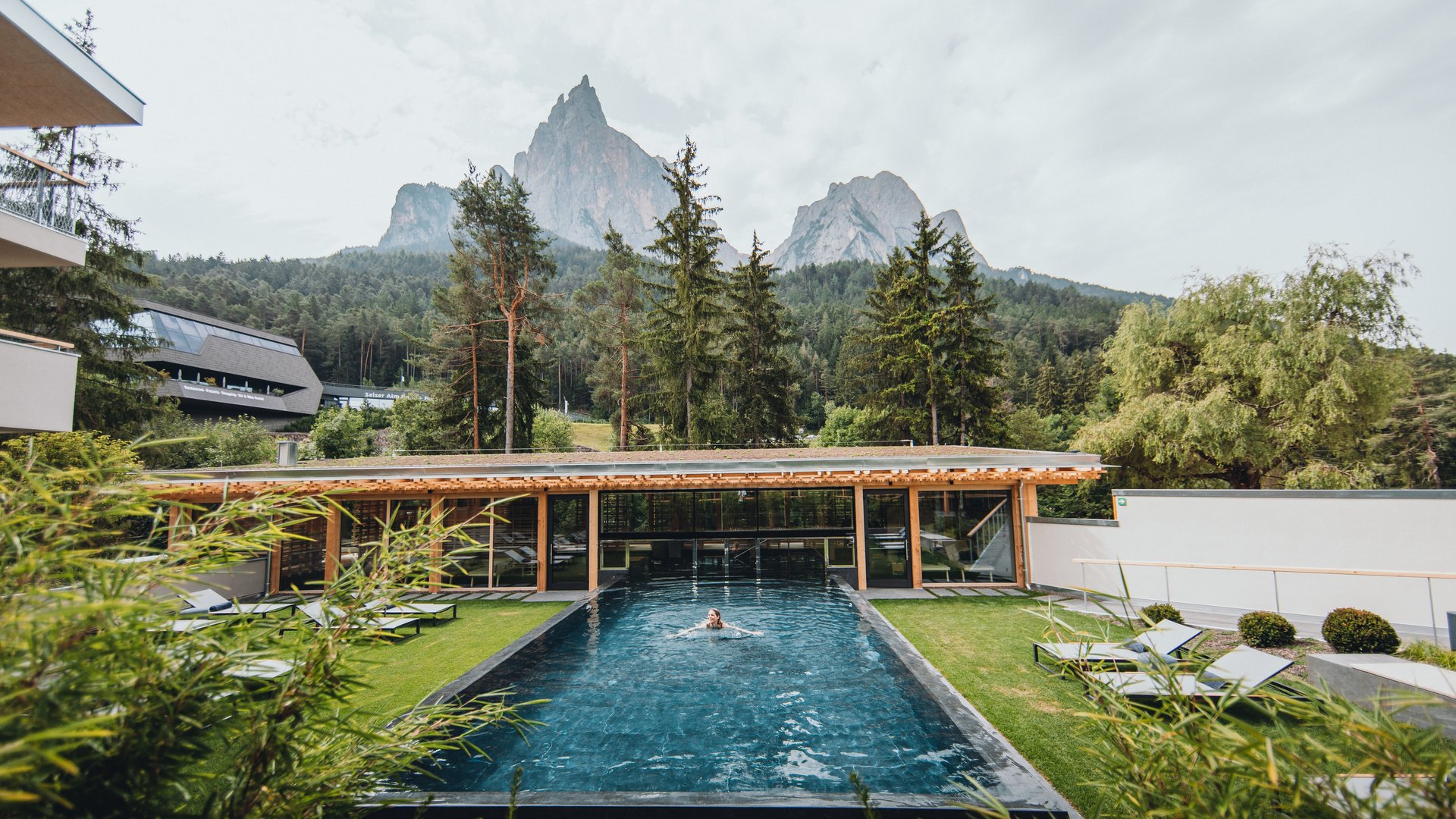 Sensoria Dolomites: Babymoon in Südtirol Frau schwimmt im Außenpool mit Bergkulisse und Bäumen im Hintergrund