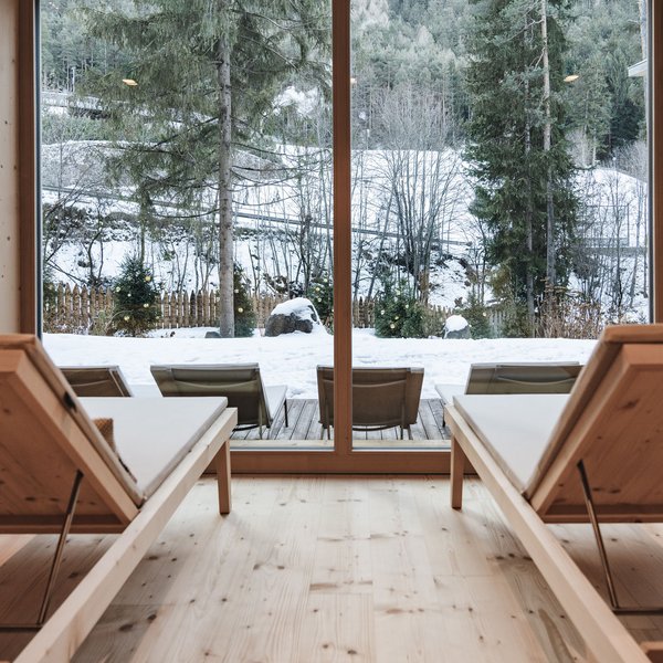 Hotel in mezzo alla natura: area spa del Sensoria Dolomites Lettini in legno con vista su alberi di Natale innevati fuori