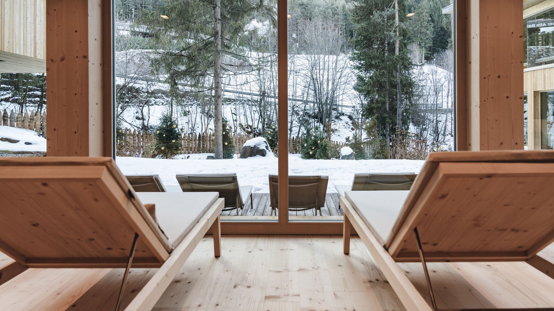 Day Spa in Südtirol – Wellness für die Seele Holzliegestühle im Raum mit Blick auf verschneite Tannenbäume draußen