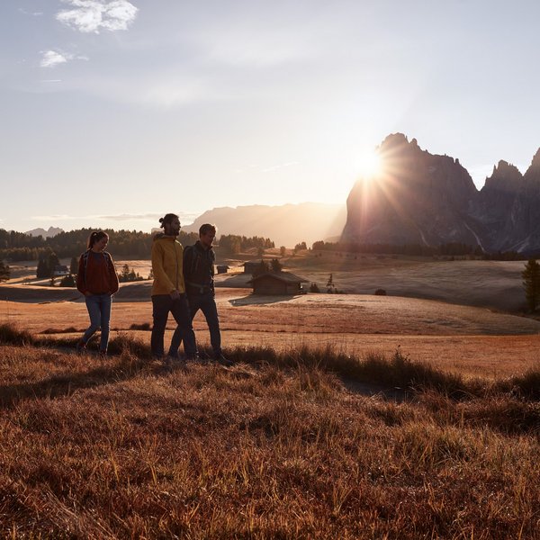 Sensoria Dolomites: much more than a hotel in South Tyrol Three hikers walking at sunset in an autumn landscape with mountains