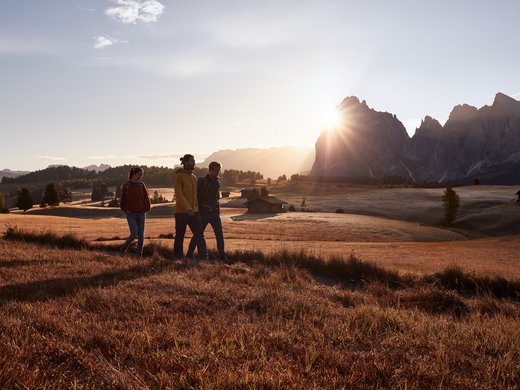 A summer holiday in the mountains Three hikers walking at sunset in an autumn landscape with mountains
